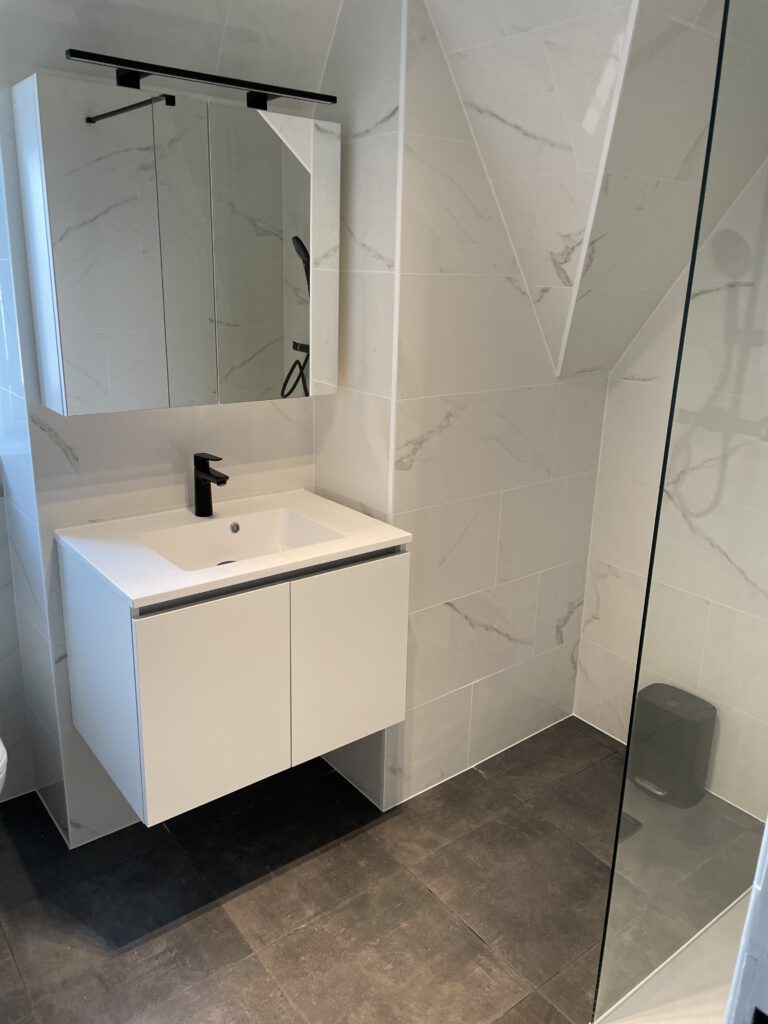 Badkamer met zwevend wit meubel, spiegelkast en een inloopdouche met glazen wand