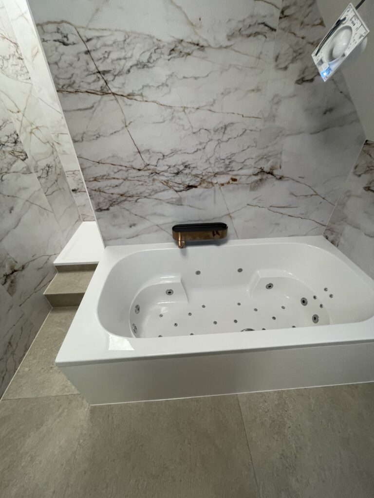 Ruim ligbad met marmerlook tegels in een gerenoveerde badkamer